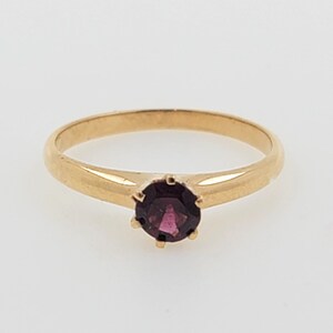 May include: A simple gold band ring with a single round purple gemstone.