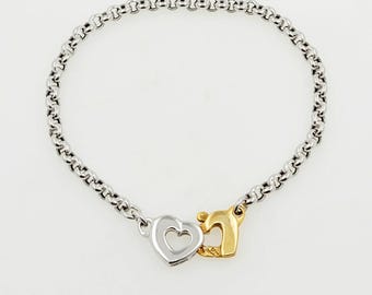 Op de afbeelding: Een zilveren kettingarmband met een bedel in de vorm van twee harten. Eén hart is zilver en het andere is goud.