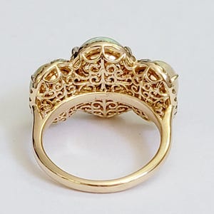 May include: A gold ring with three opal stones set in a filigree design. The ring is shown from the back, revealing the intricate details of the band.