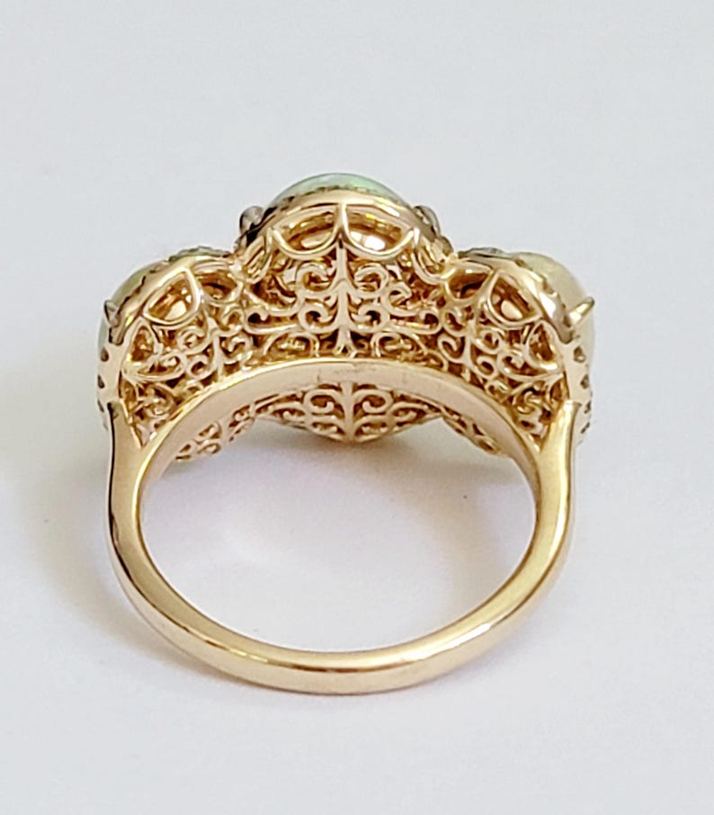 May include: A gold ring with three opal stones set in a filigree design. The ring is shown from the back, revealing the intricate details of the band.