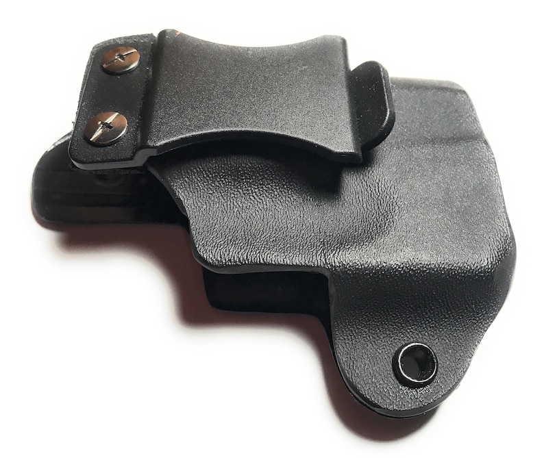 Puede incluir: Funda de pl&aacute;stico negro con un clip para cintur&oacute;n y dos tornillos plateados. La funda tiene una superficie texturizada y un peque&ntilde;o agujero en la parte inferior.