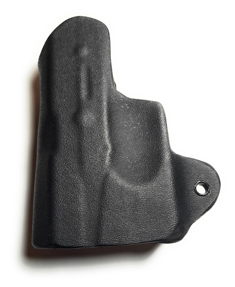 Puede incluir: Funda de cuero negra para una pistola. La funda tiene una superficie texturizada y un solo agujero en el lateral.