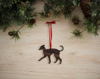 May include: A wooden ornament shaped like a dog, hanging from a red ribbon against a wood background. The ornament is a silhouette of a dog, with a dark brown wood finish.