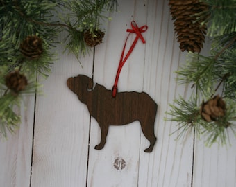 May include: A wooden Christmas ornament shaped like a dog, painted brown. The ornament has a red ribbon attached to the top.
