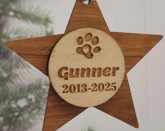 May include: Wooden star-shaped ornament with a paw print and the name "Gunner" and dates "2013-2025" engraved on a circular wooden piece. The ornament is suspended by a natural twine string, perfect for pet memorial or holiday decor.