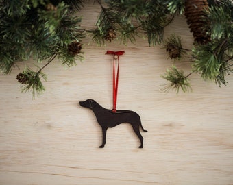 May include: A black silhouette of a dog, possibly a hound, is cut out of wood and hangs from a red ribbon. The ornament is perfect for a Christmas tree or a dog lover's home decor.