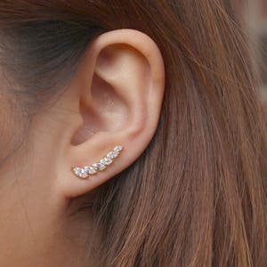 May include: A gold ear cuff with a row of clear marquise-shaped stones. The ear cuff is curved and sits on the upper part of the ear.
