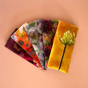 Könnte beinhalten: Ein Set mit sechs Augenmasken aus Samtstoff mit Blumenprints. Die Augenmasken sind in verschiedenen Farben, darunter Gelb, Orange, Rot, Lila, Grün und Weiß.