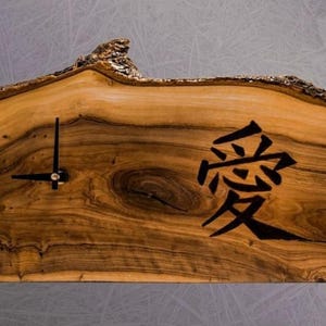 May include: A wooden wall clock with a natural edge. The clock face is a light brown color with dark brown wood grain. The clock hands are black, and the word "love" is written in Japanese characters.