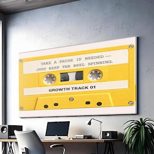 May include: A large yellow cassette tape art print with the text "TAKE A PAUSE IF NEEDED - JUST KEEP THE REEL SPINNING. GROWTH TRACK 01" hangs above a desk. The office space includes a computer, speakers, and plants.