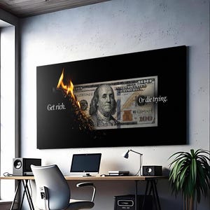 May include: A modern office setting with a large black framed artwork featuring a burning $100 bill. The artwork has the text "Get rich. Or die trying." A wooden desk with a laptop, speakers, and a desk lamp is in front of the artwork.