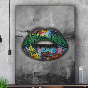 Könnte beinhalten: Leinwanddruck mit einem Lippenpaar im Graffiti-Design. Die Lippen sind grün mit schwarzer Schattierung und mit farbenfroher Graffiti-Kunst gefüllt. Der Hintergrund ist ein strukturierter Grauton.