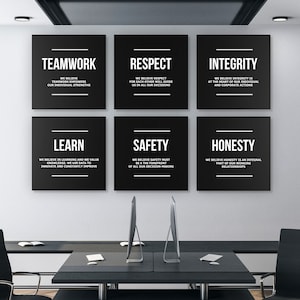May include: Six black square signs with white text on a white wall. The signs have the words "Teamwork", "Respect", "Integrity", "Learn", "Safety", and "Honesty" with a short description of each value below.