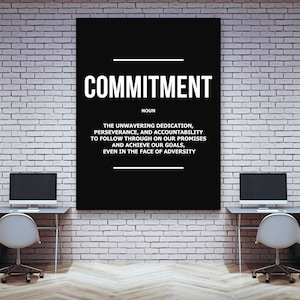 May include: A black rectangular wall art piece with the word "COMMITMENT" in large white letters. Below, the definition of commitment is written in white text. The artwork hangs on a white brick wall.