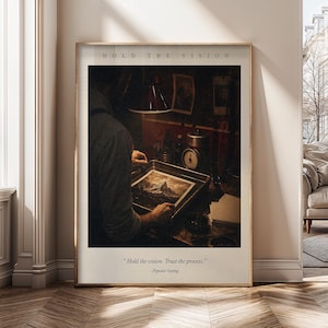 May include: A framed wall art print featuring a dark, moody scene of a person developing a photograph in a tray. The text HOLD THE VISION appears at the top, and the quote Hold the vision. Trust the process. - Popular Saying is at the bottom.