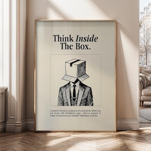 Może przedstawiać: Oprawiony wydruk artystyczny z napisem "Think Inside The Box". Czarno-biała ilustracja przedstawia osobę w garniturze z pudełkiem zamiast głowy. Wydruk zawiera cytat o kreatywności i ograniczeniach. Grafika jest oprawiona w złotą ramę.