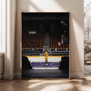 May include: A framed print featuring a basketball player on a court. The player, in a yellow and black uniform, stands with a basketball. Text on the image reads "the support" and "the grind". The background shows empty stadium seating.