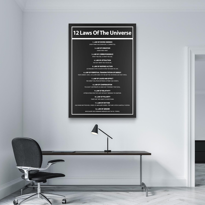 May include: A framed black and white poster titled "12 Laws Of The Universe" hangs on a white wall. The poster lists twelve laws in white text. A black desk, chair, and lamp are in front of the poster.
