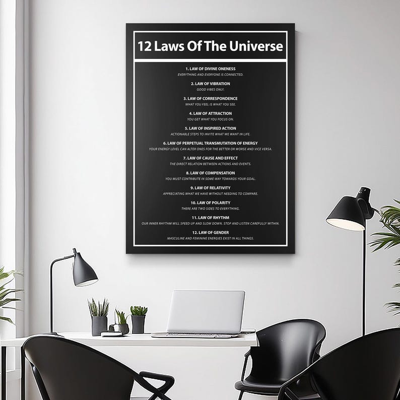 May include: A framed black and white print titled "12 Laws Of The Universe." The print lists twelve laws with brief descriptions. The print is displayed on a white wall in a modern office setting, with a desk, laptop, and lamps.