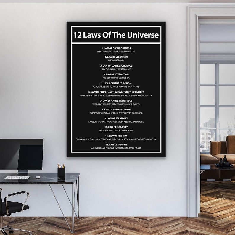 May include: A framed black and white print titled "12 Laws of the Universe." The text lists the twelve laws, including the Law of Attraction and the Law of Vibration. The print is displayed on a white wall in a room with a desk and a computer.