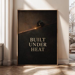 Op de afbeelding: Een verticale rechthoekige wandprint met een donkere, getextureerde achtergrond waarop een lasser langs een gloeiende oranje lijn werkt. De tekst BUILT UNDER HEAT staat in grote, vetgedrukte, lichtgekleurde hoofdletters.