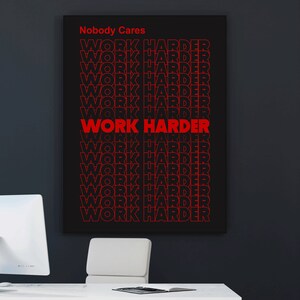 May include: Black framed poster with the words "Nobody Cares" above a repeated pattern of "WORK HARDER" in red, bold font. The poster is hanging on a dark wall above a white desk and chair.