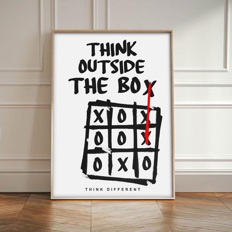 Puede incluir: Impresi&oacute;n enmarcada con la frase "THINK OUTSIDE THE BOX" en letras negras y en negrita. Debajo, un juego de tres en raya con una l&iacute;nea ganadora tachada con una "X" roja. Las palabras "THINK DIFFERENT" est&aacute;n en la parte inferior.