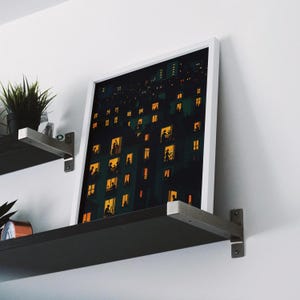 K&ouml;nnte beinhalten: Ein gerahmter Kunstdruck, der eine n&auml;chtliche Stadtlandschaft mit beleuchteten Fenstern zeigt. Das Kunstwerk verwendet eine dunkle Farbpalette mit warmem gelbem und orangefarbenem Licht, das aus den Fenstern kommt und Szenen von Menschen im Inneren andeutet. Der Druck wird auf einem Regal ausgestellt.