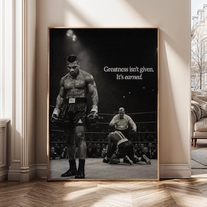 May include: A black and white poster featuring a boxing match scene with a standing boxer in the foreground and a referee and a fallen boxer in the background. The text "Greatness isn't given. It's earned." is printed in white on the right side.