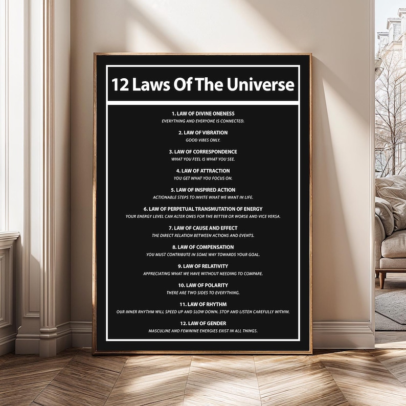 May include: A framed black and white print titled "12 Laws Of The Universe." The print lists the 12 laws with brief descriptions. The text is in a clean, sans-serif font. The frame is black and the print is displayed on a wall.