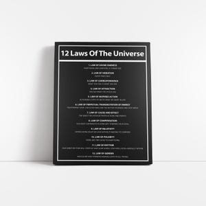 May include: A black and white framed print titled "12 Laws Of The Universe." The text lists the 12 laws, including Divine Oneness, Vibration, and Attraction. The print is displayed on a white surface.