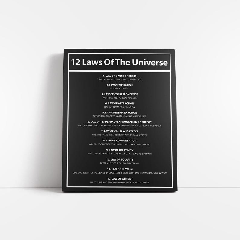 May include: A black and white framed print titled "12 Laws Of The Universe." The text lists the 12 laws, including Divine Oneness, Vibration, and Attraction. The print is displayed on a white surface.