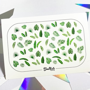 May include: A sheet of nail art stickers with a variety of green tropical leaf designs. The sheet is white with a black oval border and the text "Diem Nails" in black cursive.