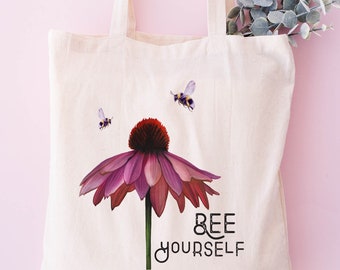 May include: A white canvas tote bag with a pink flower and bees printed on it. The text "BEE YOURSELF" is printed below the flower.