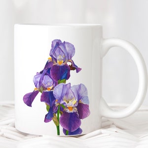May include: White ceramic mug featuring a design of purple and blue iris flowers. The mug has a white handle.