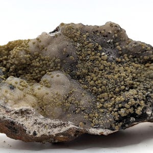 May include: A natural mineral specimen featuring a rough, irregular shape. The stone displays a mix of colors, including shades of brown, gray, and green. The surface is textured with small, rounded formations, creating a unique and organic appearance.