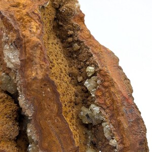 May include: A close-up of a rough, textured rock formation in shades of brown and orange. Clear, crystalline structures are embedded within the rock, catching the light. The rock's surface has a layered appearance.