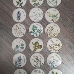 Peut inclure: Ensemble de dessous de verre ronds en céramique blanche, chacun orné d'illustrations botaniques d'herbes aromatiques. Chaque dessous de verre présente une herbe différente, comme le basilic ou le thym, avec son nom imprimé. Présentés sur une surface en bois.