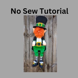 May include: A handmade leprechaun doll with a black top hat, orange beard, and green outfit. The doll has a black jacket with green trim, green pants, and black shoes with gold buckles. The text "No Sew Tutorial" is at the top.