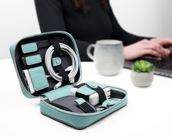 May include: A light blue leather travel case with a zipper closure, containing various electronic accessories, including a power bank, charging cables, and a USB hub.
