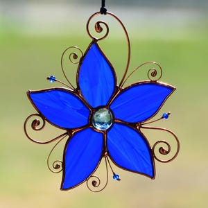 Peut inclure: Une fleur en verre teint&eacute; bleu avec des accents de fil de cuivre. La fleur a cinq p&eacute;tales et un petit bijou bleu au centre.
