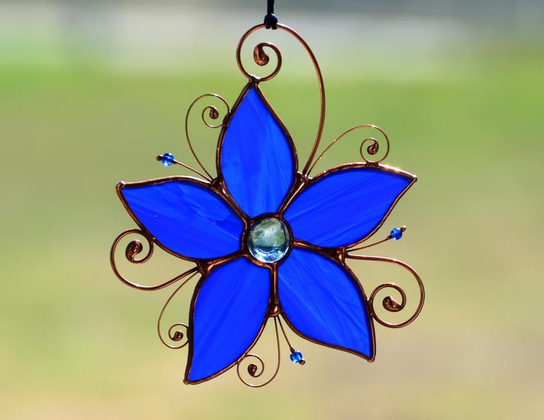 Peut inclure: Une fleur en verre teint&eacute; bleu avec des accents de fil de cuivre. La fleur a cinq p&eacute;tales et un petit bijou bleu au centre.