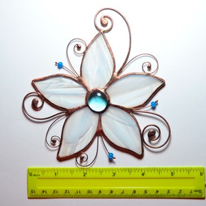 Peut inclure: Une fleur en verre blanc teint&eacute; avec un centre en verre bleu, entour&eacute;e de volutes de fil de cuivre. La fleur mesure environ 12,7 cm de large.