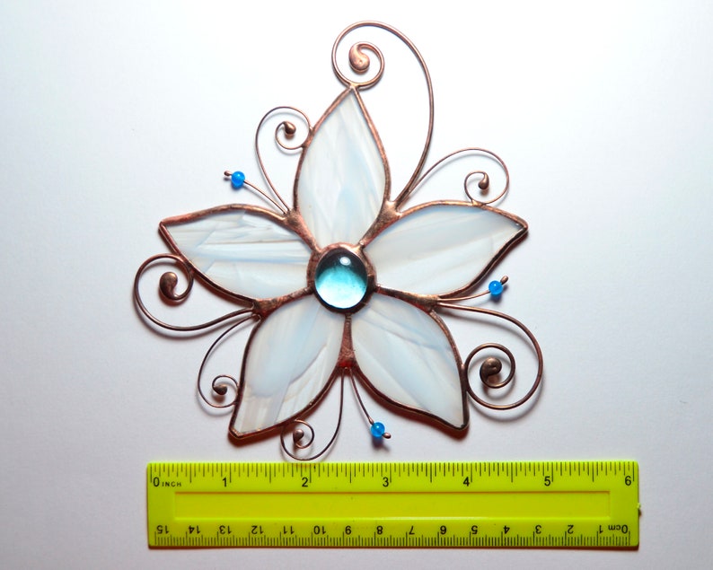Peut inclure: Une fleur en verre blanc teint&eacute; avec un centre en verre bleu, entour&eacute;e de volutes de fil de cuivre. La fleur mesure environ 12,7 cm de large.