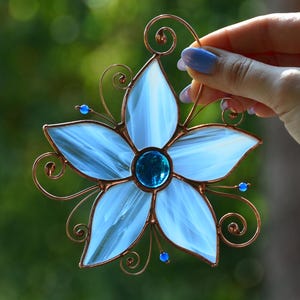 Peut inclure: Une fleur en verre teint&eacute; bleu avec un cadre en fil de cuivre et des perles de verre bleues. La fleur a cinq p&eacute;tales et un centre en verre bleu.