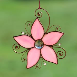 Peut inclure: Une fleur en verre teint&eacute; rose avec un cadre en fil de cuivre et un centre en verre transparent. La fleur est suspendue &agrave; une boucle de fil de cuivre.