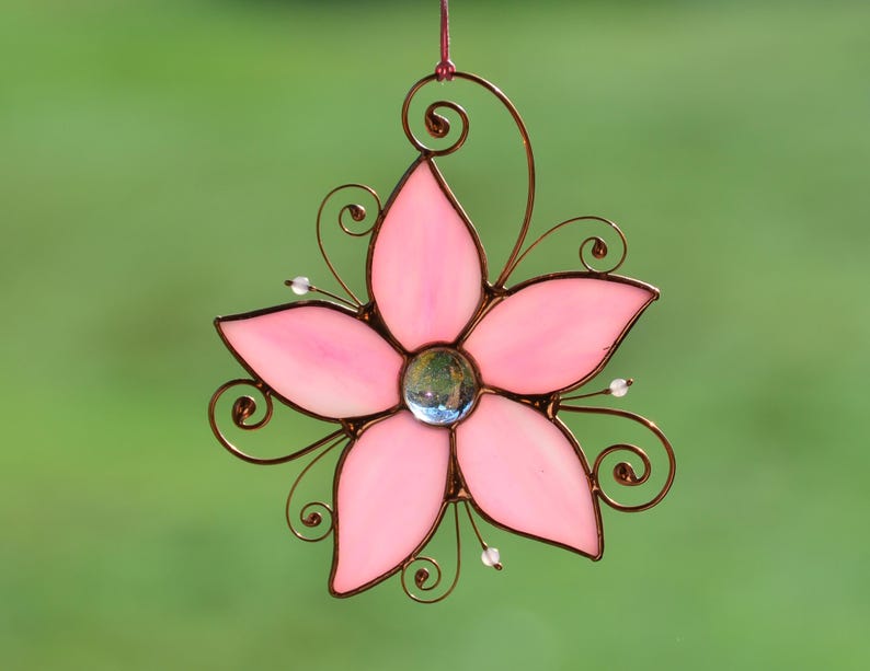 Peut inclure: Une fleur en verre teint&eacute; rose avec un cadre en fil de cuivre et un centre en verre transparent. La fleur est suspendue &agrave; une boucle de fil de cuivre.