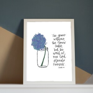 May include: A white framed print with a blue watercolor flower in a mason jar. The print features a bible verse: "The grass withers, the flower fades, but the word of our God stands forever."  - Isaiah 40:8
