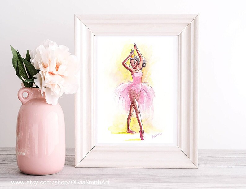 May include: Watercolor painting of a ballerina in a pink tutu and pointe shoes, framed in a white wooden frame. The artwork features a yellow and white background. A pink vase with a white flower is in the foreground.