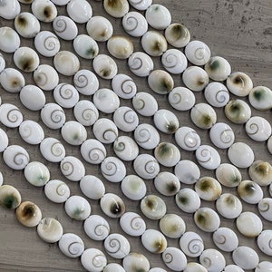 May include: A strand of white oval shell beads with brown and green swirls. The beads are strung on a white cord.